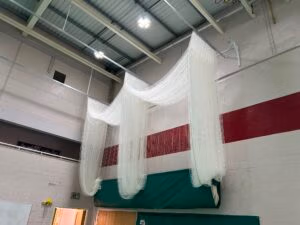 Double bay indoor cricket net system professionally installed in a sports hall with heavy-duty white cricket netting and two practice lanes.